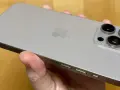 En hand håller en ljusgrå iPhone 15. Kameramodulen på baksidan har tre linser, redo att fånga dina bästa ögonblick.