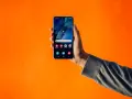 En hand håller upp en Samsung-telefon med dubbla SIM-kort mot en orange bakgrund.