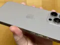 En hand håller en silverfärgad iPhone 15 Pro Max. Kameramodulen med tre linser syns tydligt.