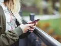 En person med blont hår håller en rosa iPhone. Snabbstart iPhone funkar inte, frustrerad över tekniken.