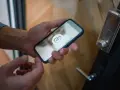 En person håller en iPhone 6 med en upplåsningsikon på skärmen, redo att låsa upp dörren.