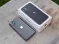 En mörkgrå iPhone 11 ligger bredvid sin vita förpackning på ett träbord. Perfekt iphone 11 storlek för handen.