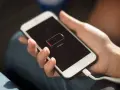 En hand håller en vit smartphone som laddas. Batteriikonen visar låg laddning och texten "Charging..." syns.