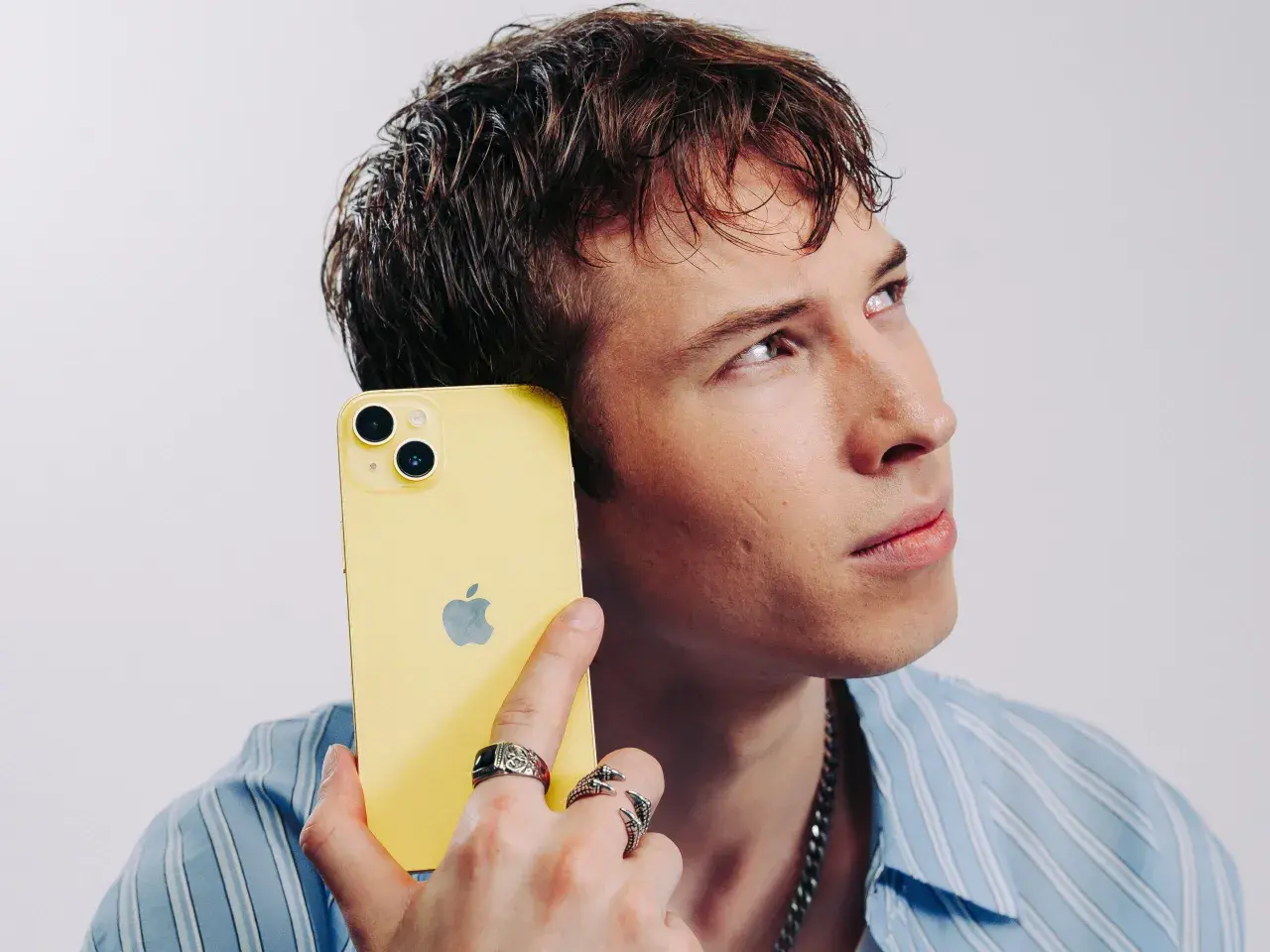 Ung man med gul iPhone mot örat, ser fundersam ut. Kanske är det dåligt ljud i iPhonen som gör honom bekymrad.