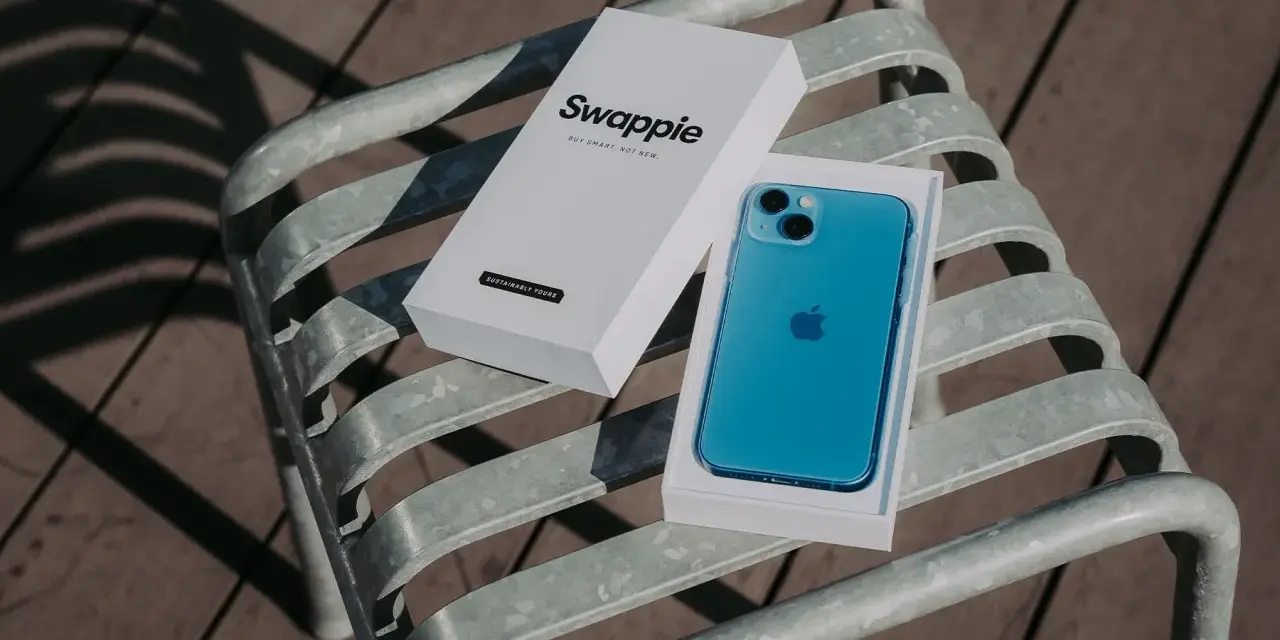 En blå iPhone 13 med Swappie-förpackning på en bänk. Denna iPhone 13 kamera är redo att fånga dina minnen.