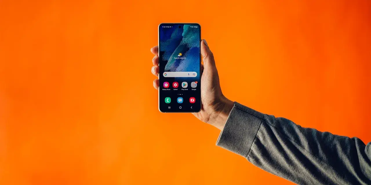 En hand håller upp en Samsung-telefon med dubbla SIM-kort mot en orange bakgrund.