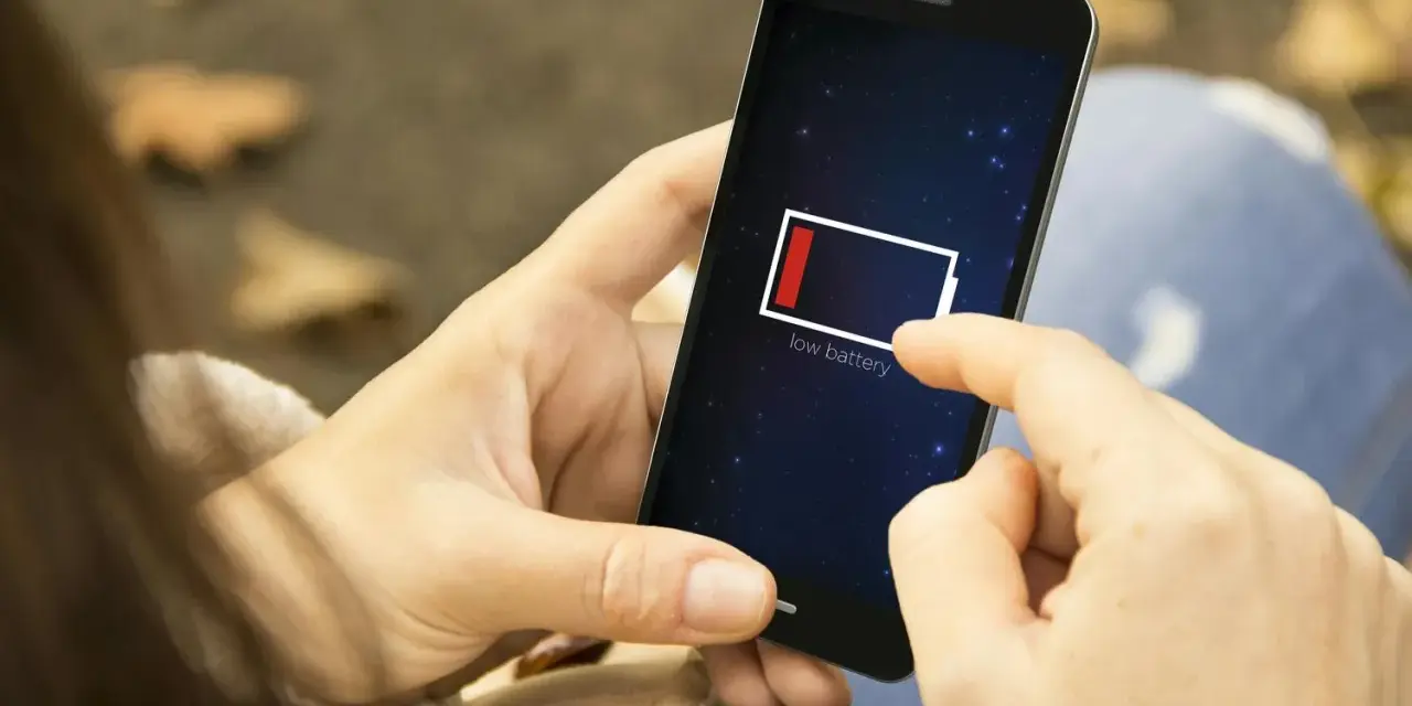 En person håller en mobil med lågt batteri. Det är mörkt ute, som om mobilen drar batteri på natten.