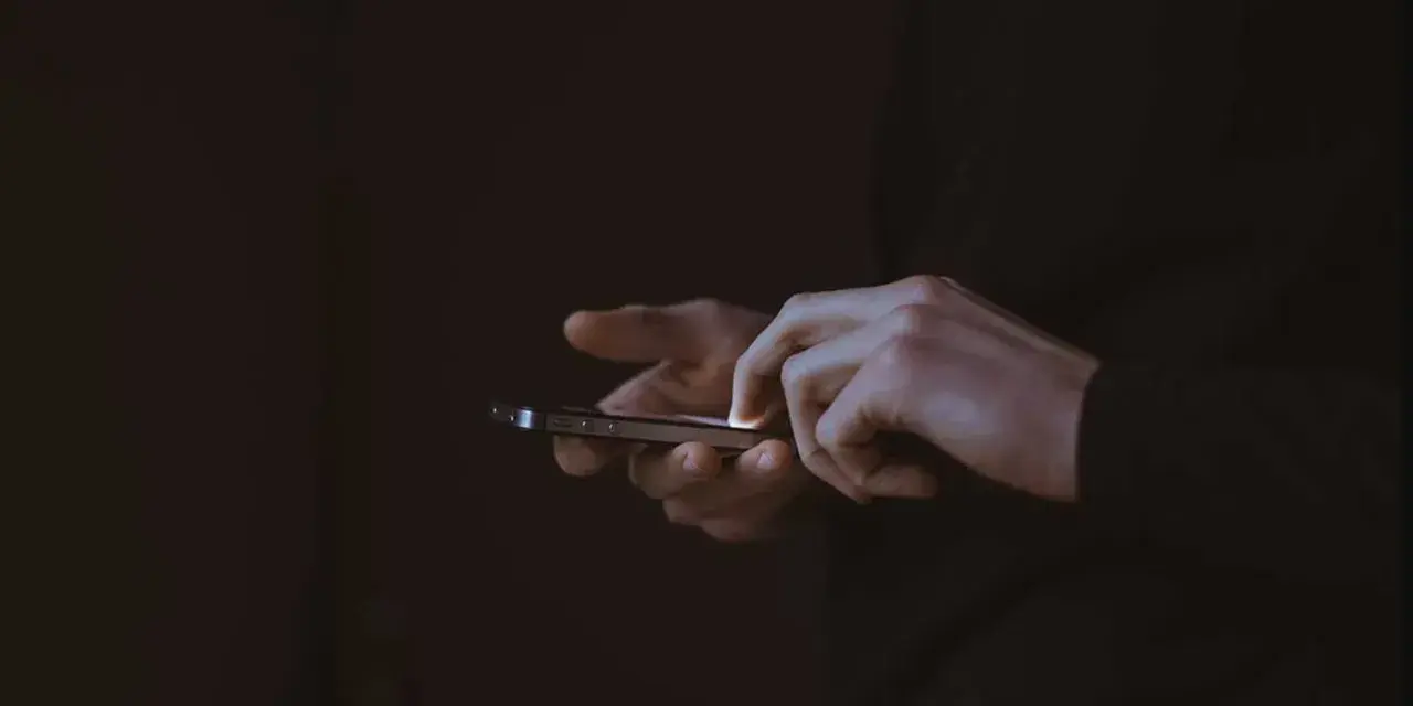 Händer som snabbtstartar en iPhone i mörkret.