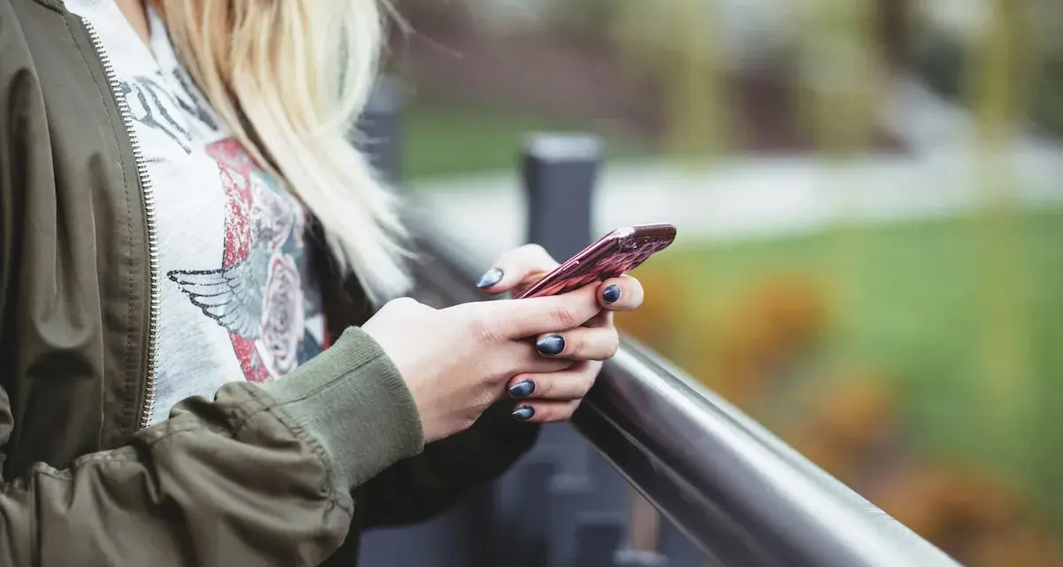En person med blont hår håller en rosa iPhone. Snabbstart iPhone funkar inte, frustrerad över tekniken.