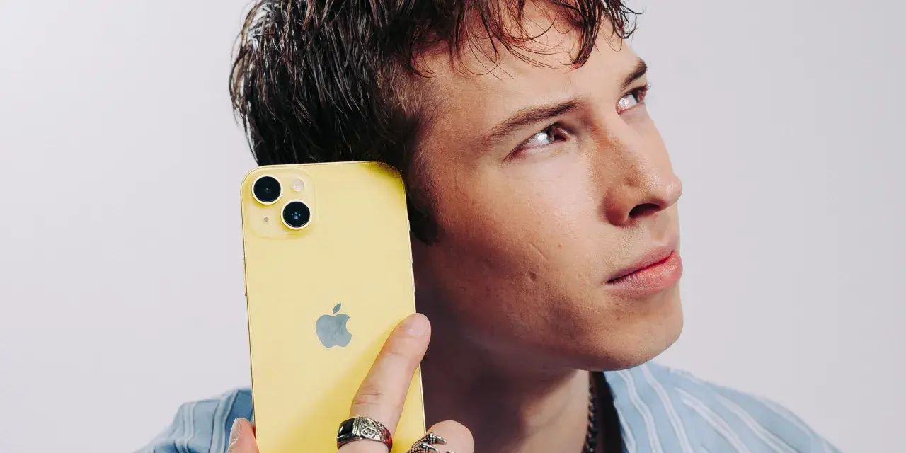 Ung man med gul iPhone mot örat, ser fundersam ut. Kanske är det dåligt ljud i iPhonen som gör honom bekymrad.