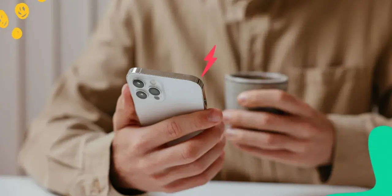 En person håller en iPhone och en mugg. En blixtsymbol indikerar att batterikapacitet iPhone är låg.