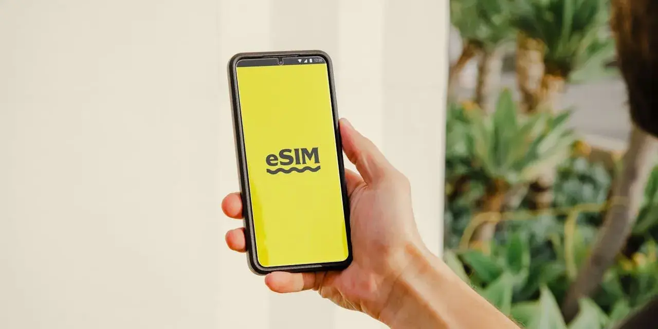 En hand håller en telefon med en gul skärm som visar "eSIM". Dags att byta SIMkort till ett eSIM för en smidigare upplevelse.
