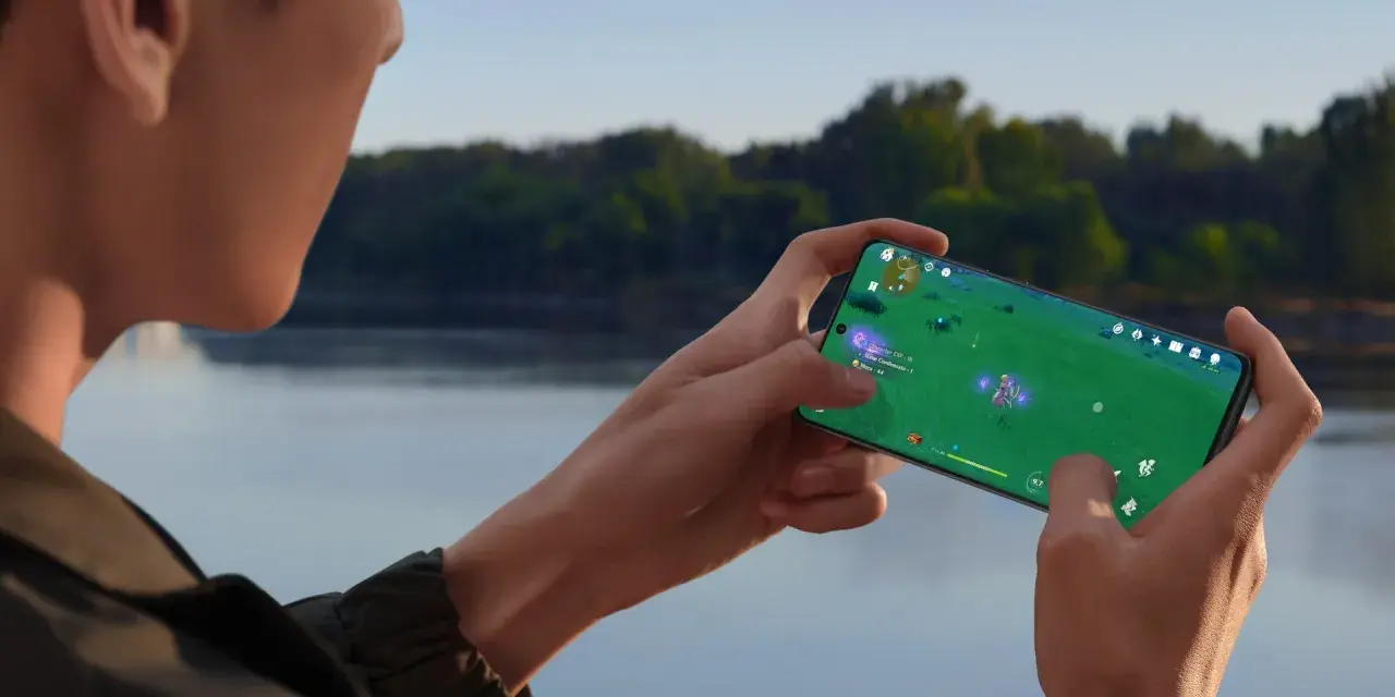 Person spelar mobilspel vid vattnet. Telefonen blir varm och drar batteri, men spelet är fängslande.