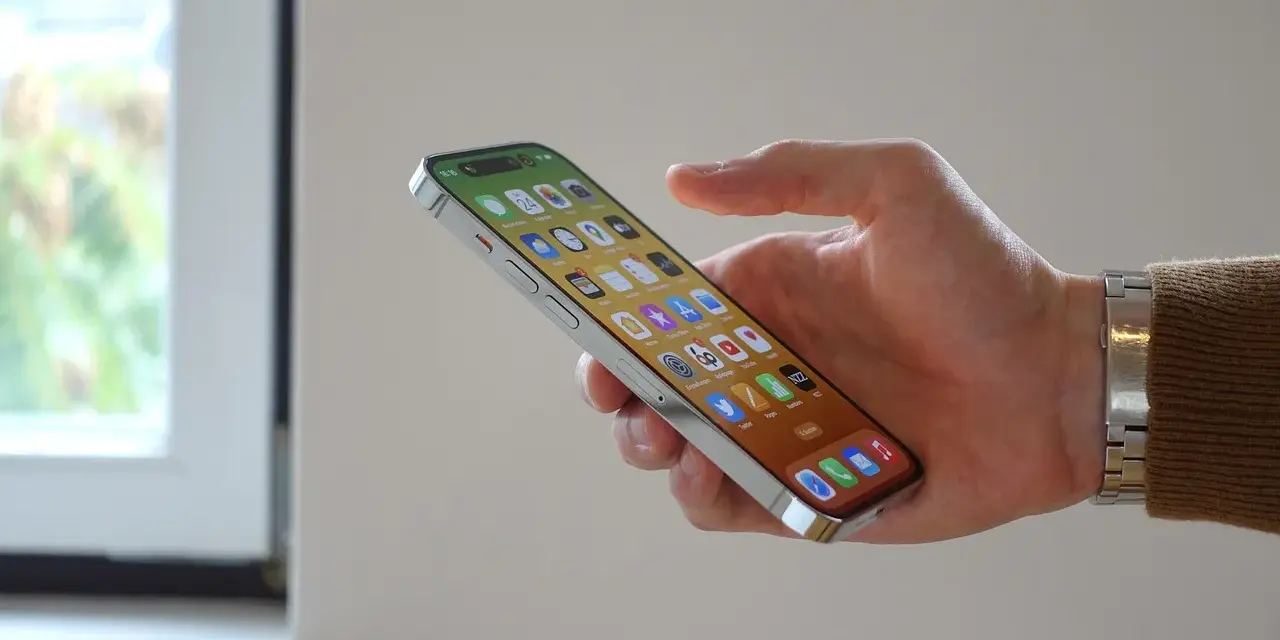 En hand håller en iPhone 12 med många appar. Bra iphone 12 batteritid gör att du kan använda den hela dagen.