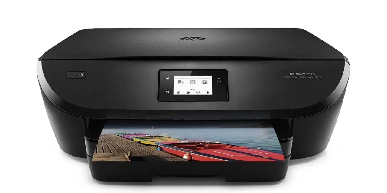 Svart HP Envy 5540-skrivare som skriver ut ett foto av färgglada båtar på en brygga. Enkel att skriva ut från iPhone.