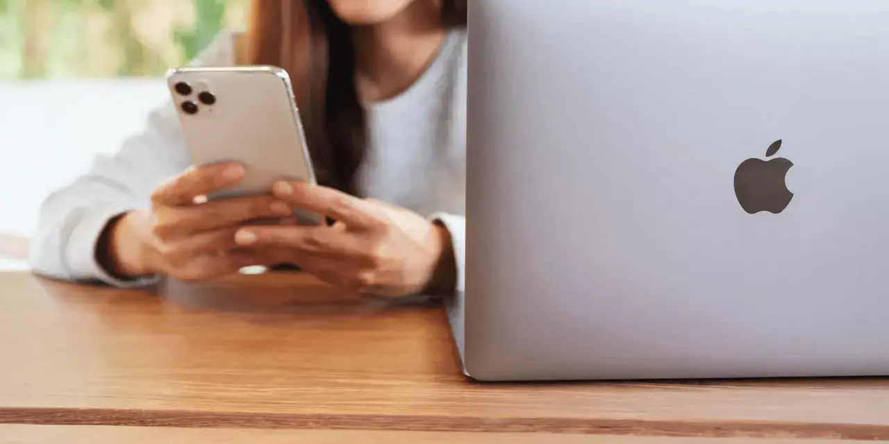 Person använder en iPhone för att skicka bilder från Samsung till iPhone. En MacBook ligger bredvid.