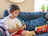 Barnet tittar fascinerat på en smartphone, med en leksaksbrandbil bredvid.