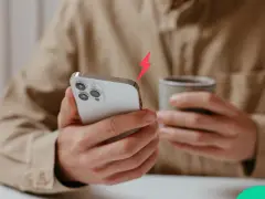 En person håller en iPhone och en mugg. En blixtsymbol indikerar att batterikapacitet iPhone är låg.