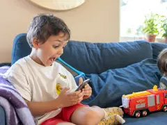 Barnet tittar fascinerat på en smartphone, med en leksaksbrandbil bredvid.