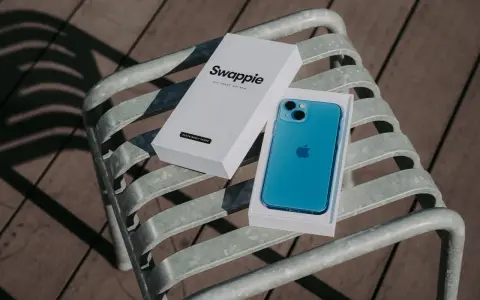 En blå iPhone 13 med Swappie-förpackning på en bänk. Denna iPhone 13 kamera är redo att fånga dina minnen.