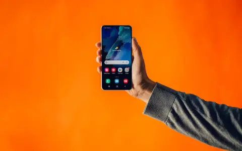 En hand håller upp en Samsung-telefon med dubbla SIM-kort mot en orange bakgrund.