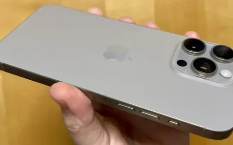 En hand håller en silverfärgad iPhone 15 Pro Max. Kameramodulen med tre linser syns tydligt.