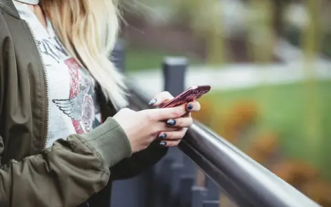 En person med blont hår håller en rosa iPhone. Snabbstart iPhone funkar inte, frustrerad över tekniken.