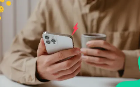En person håller en iPhone och en mugg. En blixtsymbol indikerar att batterikapacitet iPhone är låg.