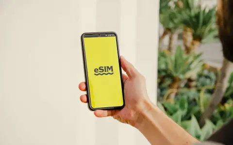 En hand håller en telefon med en gul skärm som visar "eSIM". Dags att byta SIMkort till ett eSIM för en smidigare upplevelse.