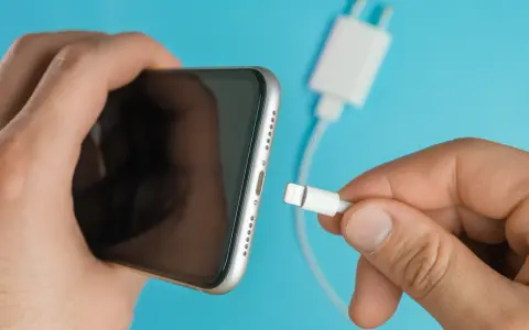 En hand håller en iPhone och en laddkabel. Var försiktig med vatten i ladduttaget på din iPhone.
