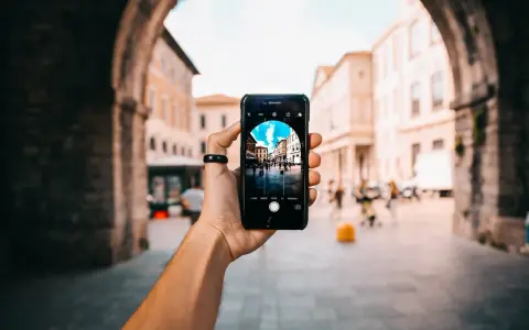 En hand håller upp en iPhone för att identifiera person på bild. Telefonen visar en livlig stadsgata med byggnader och människor.