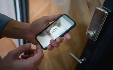 En person håller en iPhone 6 med en upplåsningsikon på skärmen, redo att låsa upp dörren.