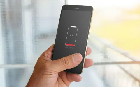 En hand håller en mobil med 3% batteri. Bakgrunden visar suddiga appaktiviteter.