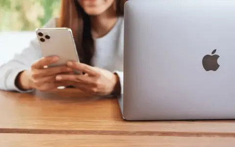 Person använder en iPhone för att skicka bilder från Samsung till iPhone. En MacBook ligger bredvid.