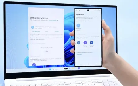 En hand håller en Samsung-telefon framför en laptop. Laptopen visar ett fönster för filöverföring, vilket underlättar att byta från iPhone till Samsung.