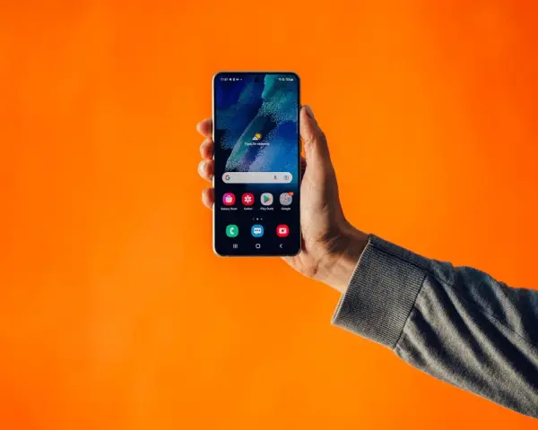 En hand håller upp en Samsung-telefon med dubbla SIM-kort mot en orange bakgrund.