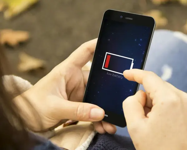 En person håller en mobil med lågt batteri. Det är mörkt ute, som om mobilen drar batteri på natten.