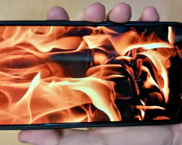 En hand håller en iPhone med en flammande eld som bakgrundsbild. Det ser ut som att iphone blir varm.