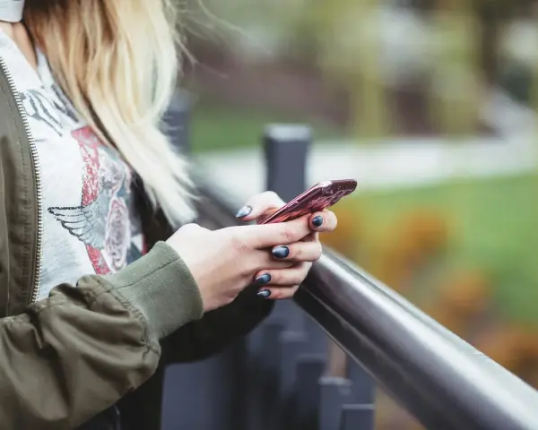 En person med blont hår håller en rosa iPhone. Snabbstart iPhone funkar inte, frustrerad över tekniken.