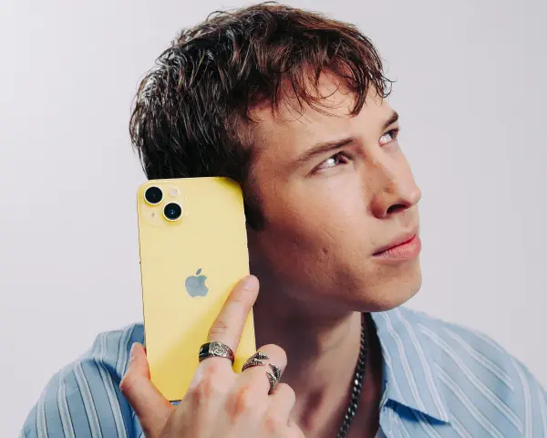 Ung man med gul iPhone mot örat, ser fundersam ut. Kanske är det dåligt ljud i iPhonen som gör honom bekymrad.