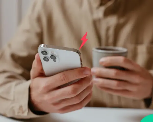 En person håller en iPhone och en mugg. En blixtsymbol indikerar att batterikapacitet iPhone är låg.