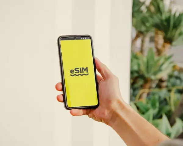 En hand håller en telefon med en gul skärm som visar "eSIM". Dags att byta SIMkort till ett eSIM för en smidigare upplevelse.