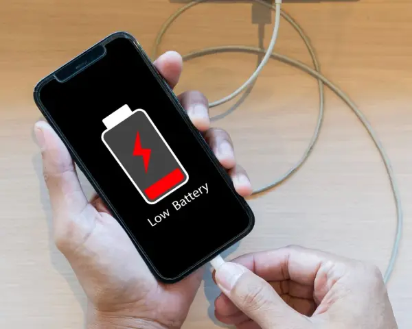 En person kopplar in sin mobil för att ladda mobilen på natten. Batteriikonen visar låg nivå.