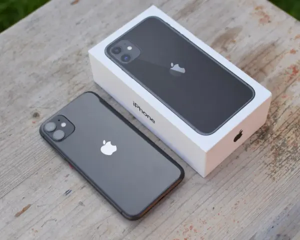 En mörkgrå iPhone 11 ligger bredvid sin vita förpackning på ett träbord. Perfekt iphone 11 storlek för handen.