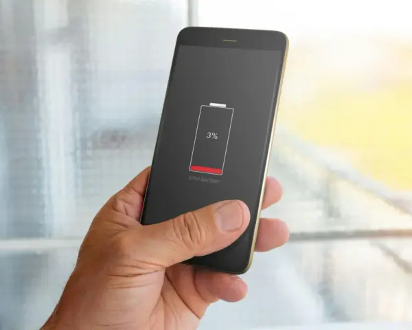 En hand håller en mobil med 3% batteri. Bakgrunden visar suddiga appaktiviteter.