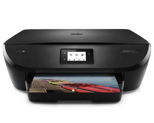 Svart HP Envy 5540-skrivare som skriver ut ett foto av färgglada båtar på en brygga. Enkel att skriva ut från iPhone.