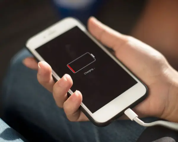 En hand håller en vit smartphone som laddas. Batteriikonen visar låg laddning och texten "Charging..." syns.