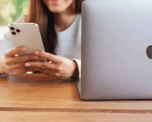 Person använder en iPhone för att skicka bilder från Samsung till iPhone. En MacBook ligger bredvid.