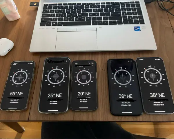 Fem iPhones visar kompass-appar. En laptop och AirPods ligger bredvid.