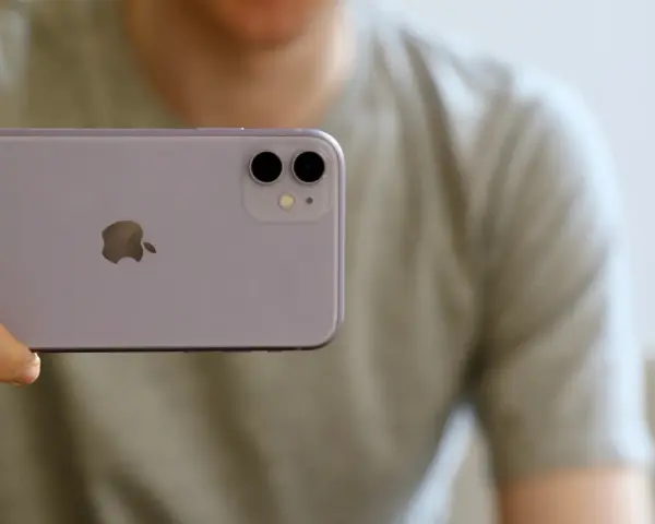 En person håller upp en lila iPhone 11. Man ser tydligt den dubbla iphone 11 kameran på baksidan.